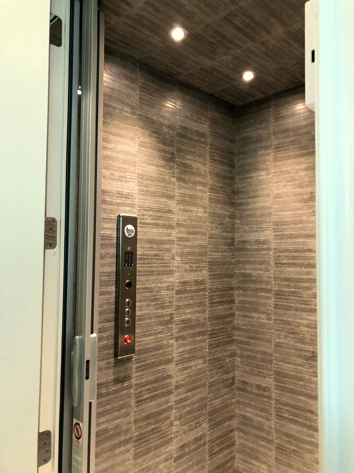 Private elevator cab, walls and ceiling. Textured wallcovering wrapped around a working cab, ceiling included, with seams landing on the panel lines.