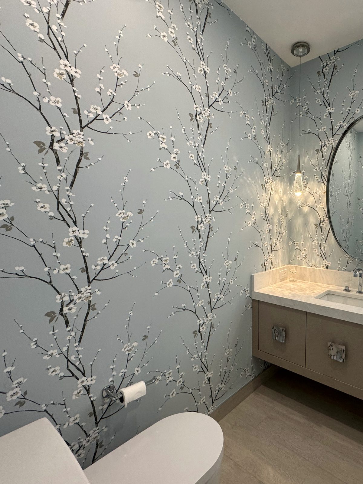 Blossom powder room. Large-scale branch pattern centered on the vanity wall so the composition reads from the doorway.